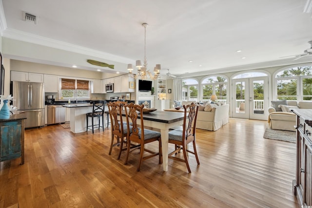 dining room with visible vents, crown molding, ceiling fan with notable chandelier, french doors, and light wood-style floors