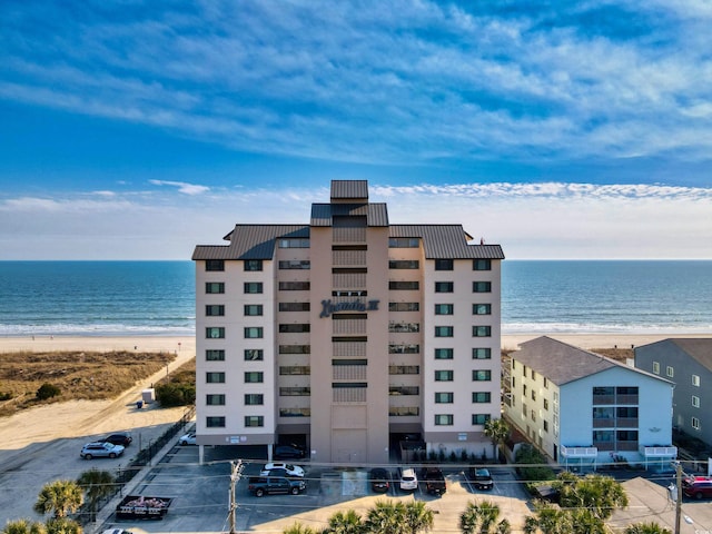 view of property featuring a water view, uncovered parking, and a view of the beach