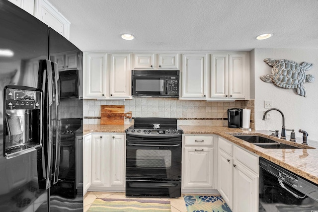 kitchen with tasteful backsplash, light stone countertops, white cabinets, black appliances, and a sink