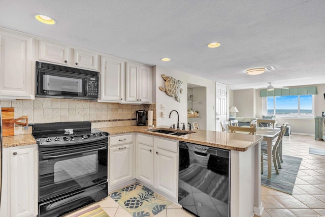 kitchen with light tile patterned floors, decorative backsplash, a peninsula, black appliances, and a sink