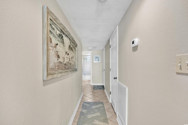 hall featuring light tile patterned floors, baseboards, visible vents, a textured ceiling, and a textured wall