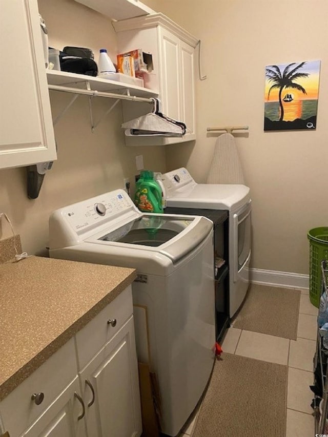 laundry area featuring light tile patterned floors, baseboards, cabinet space, and washing machine and clothes dryer