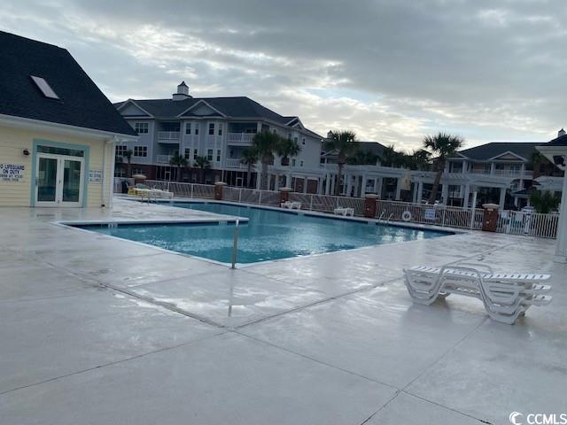 community pool featuring french doors, a residential view, a patio area, and fence