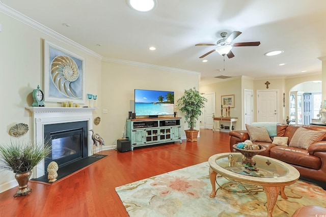 living area featuring arched walkways, a glass covered fireplace, crown molding, and wood finished floors