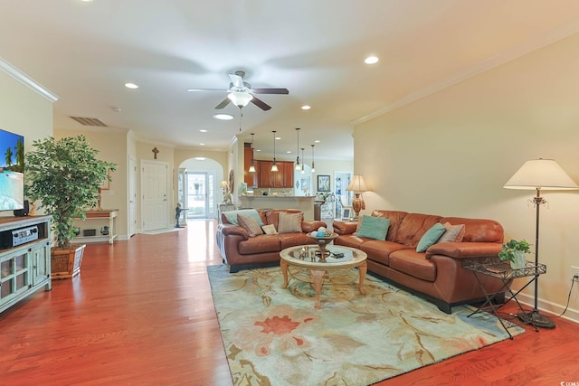 living area with arched walkways, visible vents, ornamental molding, and wood finished floors