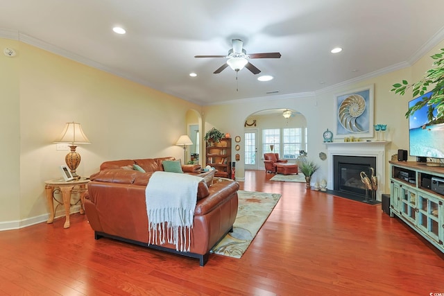 living room with arched walkways, wood finished floors, a fireplace with flush hearth, and ornamental molding