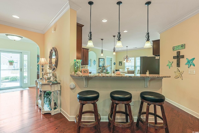 kitchen featuring dark wood-style floors, arched walkways, freestanding refrigerator, and ornamental molding