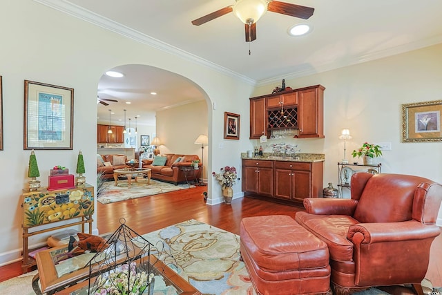 living room with dark wood finished floors, arched walkways, ceiling fan, ornamental molding, and a dry bar