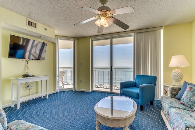 carpeted living area featuring visible vents, baseboards, a textured ceiling, and a ceiling fan