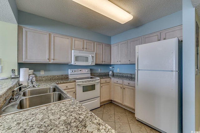 kitchen with light brown cabinetry, light tile patterned flooring, white appliances, a textured ceiling, and a sink