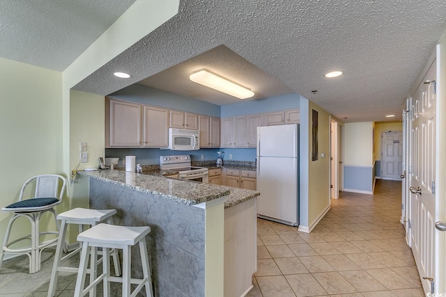 kitchen featuring white appliances, light tile patterned floors, a peninsula, a textured ceiling, and a kitchen breakfast bar