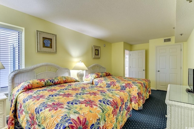 bedroom featuring visible vents, dark carpet, and a textured ceiling