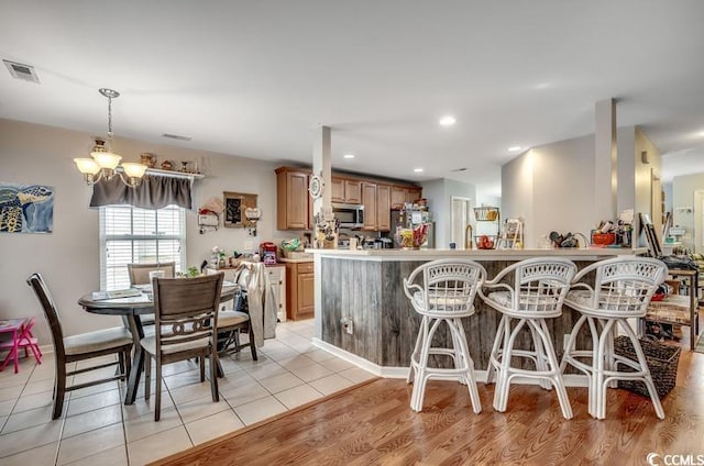 kitchen featuring visible vents, a peninsula, appliances with stainless steel finishes, a kitchen bar, and a notable chandelier