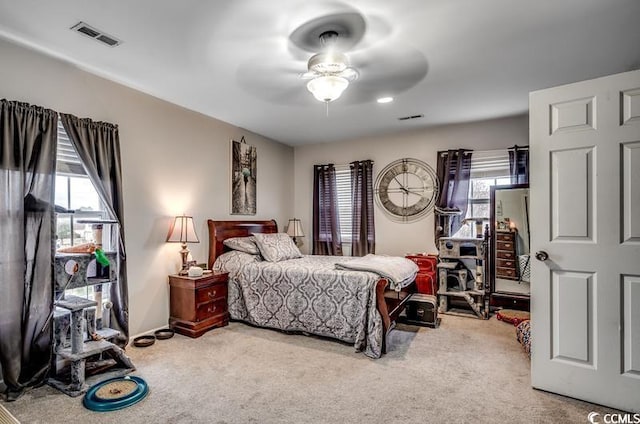 carpeted bedroom featuring visible vents, multiple windows, and a ceiling fan