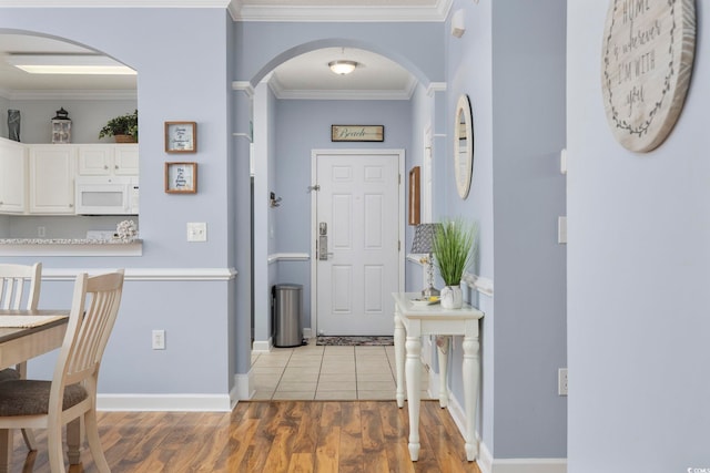 entryway with baseboards, arched walkways, light wood-type flooring, and ornamental molding