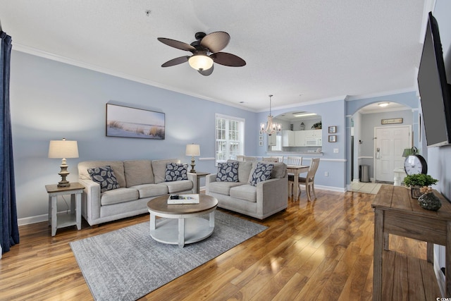 living room featuring ornamental molding, ceiling fan with notable chandelier, arched walkways, light wood finished floors, and baseboards