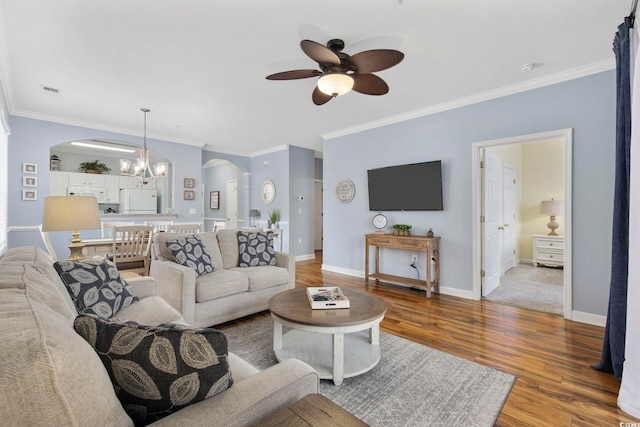 living room with wood finished floors, baseboards, arched walkways, crown molding, and ceiling fan with notable chandelier