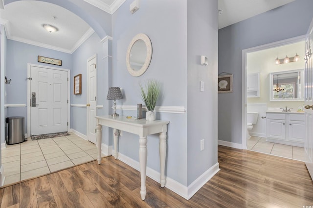 foyer with arched walkways, ornamental molding, baseboards, and wood finished floors