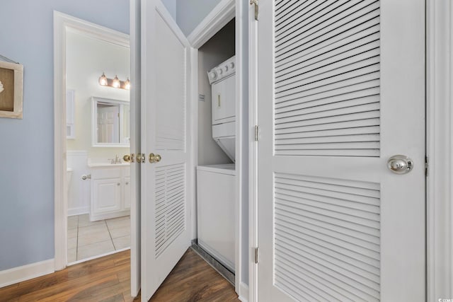 clothes washing area with laundry area, stacked washer / dryer, dark wood-style floors, and baseboards