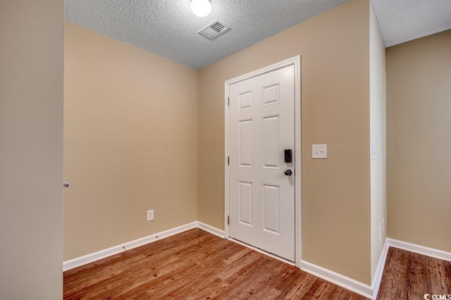 foyer featuring visible vents, baseboards, a textured ceiling, and wood finished floors