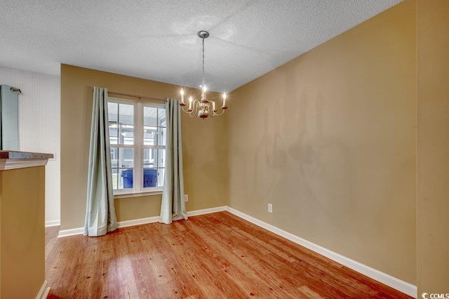 unfurnished dining area with baseboards, a notable chandelier, wood finished floors, and a textured ceiling