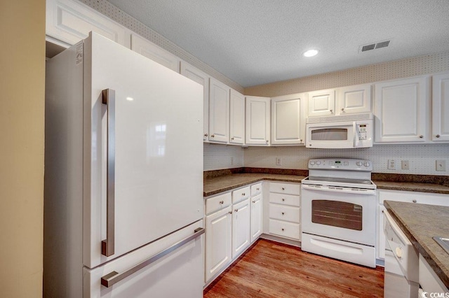 kitchen with dark countertops, visible vents, white appliances, and white cabinetry