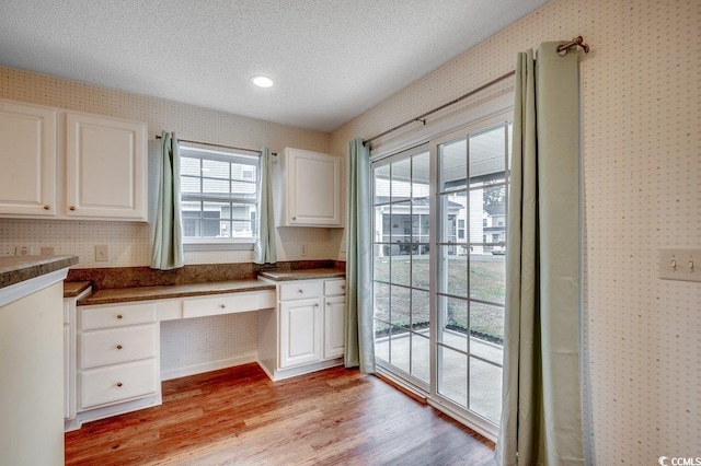 kitchen with built in study area, wallpapered walls, white cabinets, a textured ceiling, and light wood-type flooring