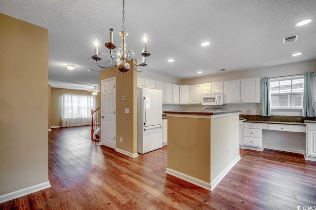 kitchen with white appliances, wood finished floors, a center island with sink, white cabinets, and a textured ceiling