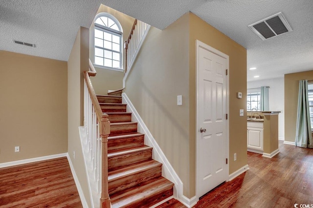 stairs with wood finished floors, visible vents, and baseboards