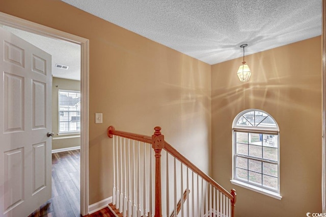 hall with visible vents, baseboards, dark wood finished floors, a textured ceiling, and an upstairs landing