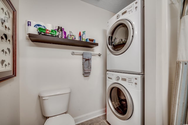 clothes washing area with tile patterned floors, baseboards, laundry area, and stacked washing maching and dryer