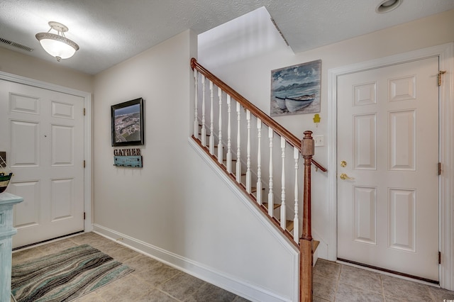 entryway featuring visible vents, a textured ceiling, stairway, light tile patterned floors, and baseboards