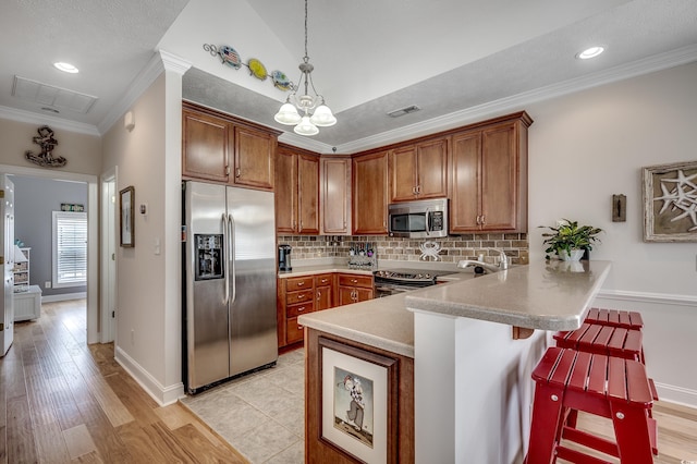 kitchen featuring tasteful backsplash, decorative light fixtures, ornamental molding, appliances with stainless steel finishes, and a peninsula