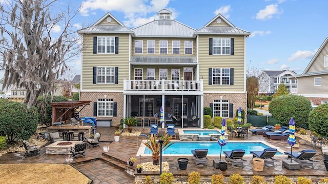 rear view of house with brick siding, a fire pit, a patio, and a sunroom