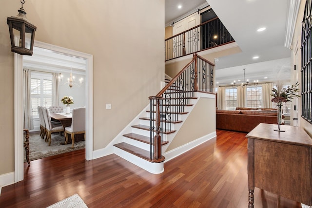 stairway with a notable chandelier, ornamental molding, wood finished floors, recessed lighting, and baseboards