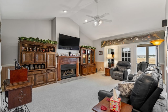 carpeted living room featuring wooden walls, a wainscoted wall, a fireplace, ceiling fan, and vaulted ceiling