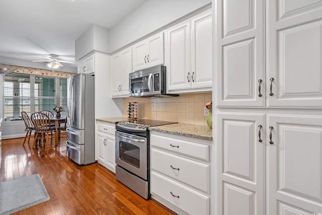 kitchen with a ceiling fan, backsplash, hardwood / wood-style floors, stainless steel appliances, and white cabinets