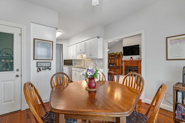 dining space featuring ceiling fan, baseboards, wood finished floors, and a fireplace