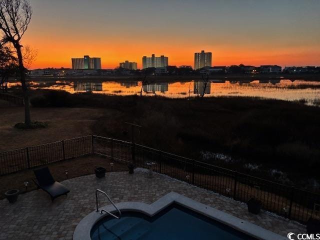 patio terrace at dusk with a city view, a water view, and fence