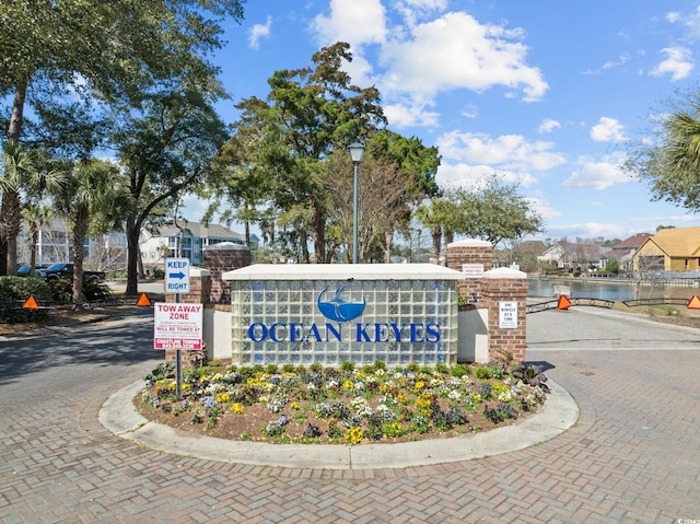 community sign with decorative driveway and a water view