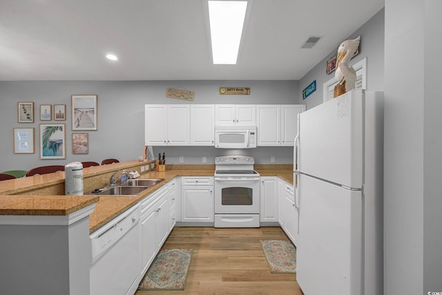 kitchen featuring visible vents, a peninsula, white cabinets, white appliances, and a sink