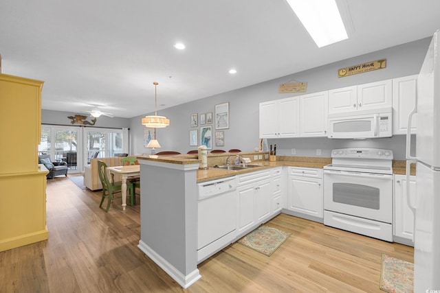 kitchen featuring open floor plan, light wood-style flooring, a peninsula, white appliances, and a sink