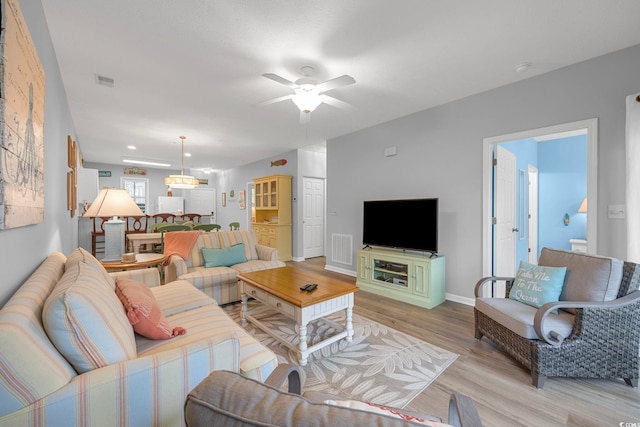 living room featuring light wood finished floors, visible vents, baseboards, and a ceiling fan