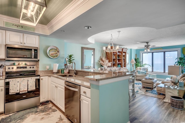 kitchen with crown molding, open floor plan, appliances with stainless steel finishes, a peninsula, and a sink