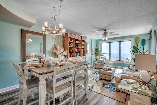 dining area featuring ceiling fan with notable chandelier, a textured ceiling, baseboards, and wood finished floors