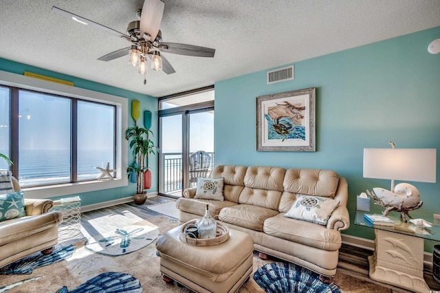 living area with visible vents, baseboards, ceiling fan, wood finished floors, and a textured ceiling