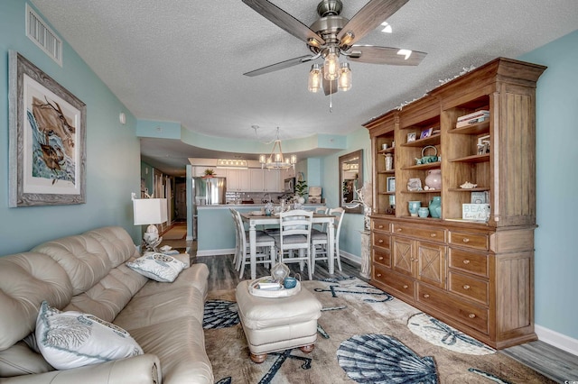 living room featuring visible vents, a textured ceiling, wood finished floors, and ceiling fan with notable chandelier