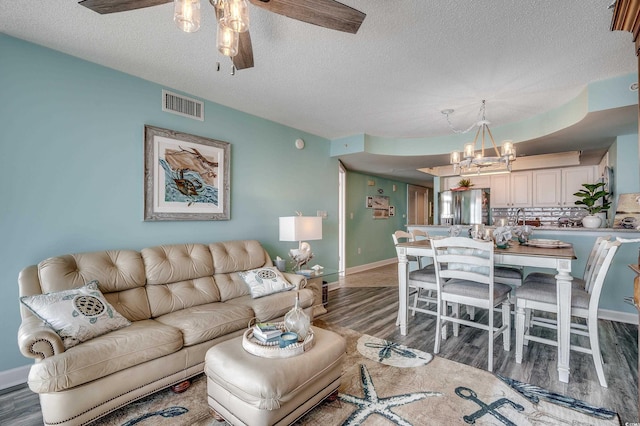 living room with ceiling fan with notable chandelier, wood finished floors, visible vents, and a textured ceiling