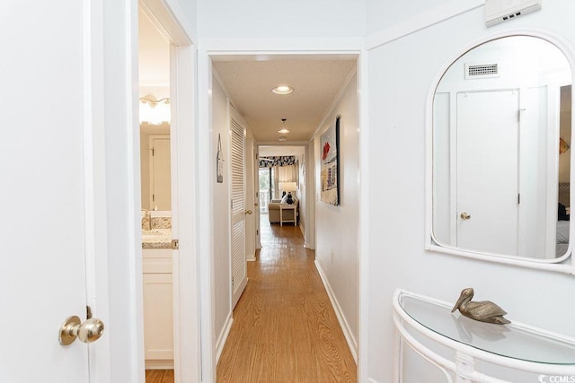 hall featuring light wood finished floors, recessed lighting, and baseboards
