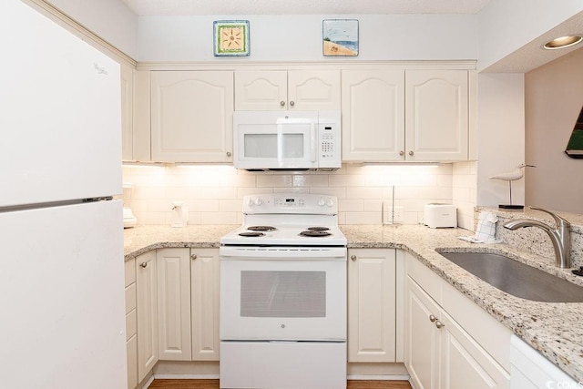 kitchen featuring white appliances, a sink, backsplash, and light stone countertops